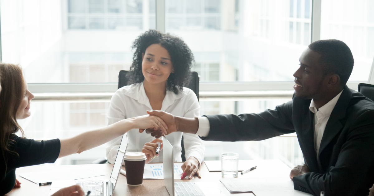 três pessoas em uma mesa de reunião e duas estão apertando as mãos.